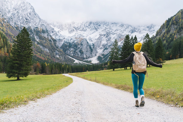 年轻貌美的女子在自然中徒步。一位快乐漂亮的女孩站在路上，眺望着远方的山景。秋季或冬季的自然风光。一名背着背包的女性在户外散步的照片。图片下载