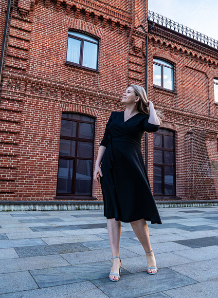 傍晚时分，一位优雅的孕妇身着时尚的黑色连衣裙，在历史悠久的砖砌建筑旁摆姿势。图片下载