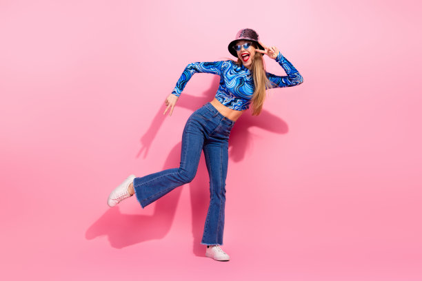 快乐迷人的年轻女孩，身穿印花蓝色上衣和牛仔裤，在粉色背景前做出俏皮姿势，用于时尚生活方式广告和购物图片图片下载
