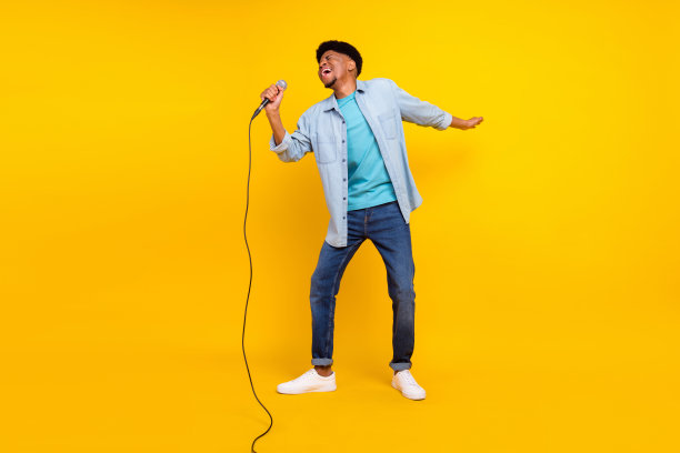 身穿牛仔衬衫、肤色黝黑的帅气男子在黄色背景下唱歌、卡拉OK和跳舞的照片图片下载