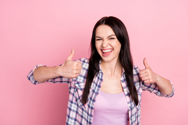 穿着格子衬衫的年轻千禧辣妹竖起大拇指，在粉色背景下展示，酷炫时尚图片下载