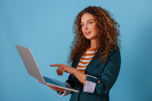 一位女高管在蓝色背景下，一边用手指着笔记本电脑屏幕上的数据一边进行展示图片下载