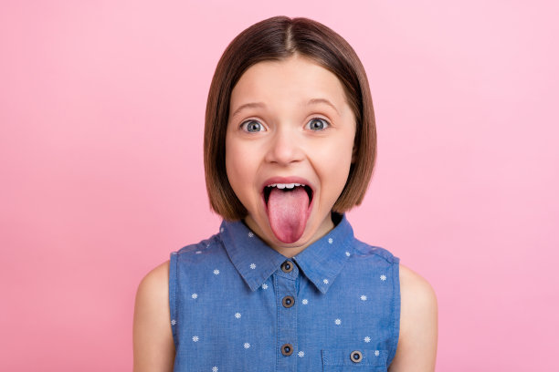 照片肖像：一个女学生吐舌头卖萌，孤立在粉彩色背景上图片下载