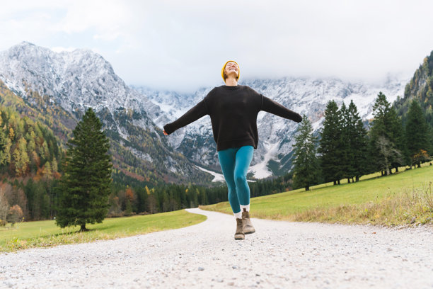年轻貌美的女子在自然中徒步。一位快乐美丽的女孩站在路上，眺望着远处的山景。秋季或冬季的自然风光。一名背着背包的女性在户外散步的照片。图片下载