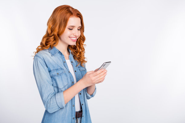 照片：一位迷人的年轻女子，笑容灿烂，手持手机，孤立在灰色背景的空白处图片下载