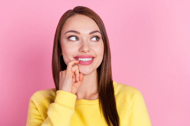 照片肖像，一个女孩微笑着咬指甲，若有所思、梦幻、好奇地看向空白空间，背景是孤立的粉彩色调图片下载