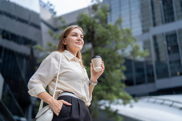 一位高加索女商人在现代屋顶花园户外行走，一位有魅力的专业年轻女员工在办公室外拿着咖啡杯，享受着都市生活，心情愉悦。图片下载