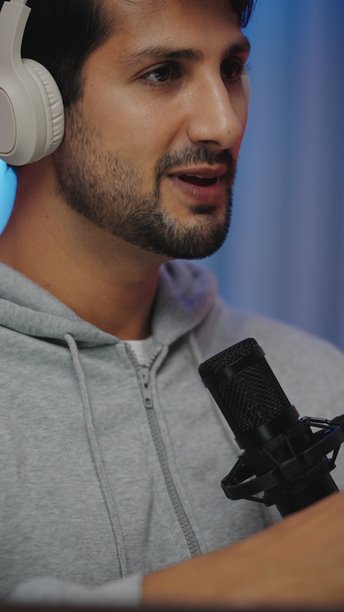 一位戴着耳机、快乐的西班牙裔拉丁裔男子正在现代家庭工作室里，使用专业麦克风录制播客，在采访中分享交流和欢笑的时刻，进行网红直播音频制作。图片下载