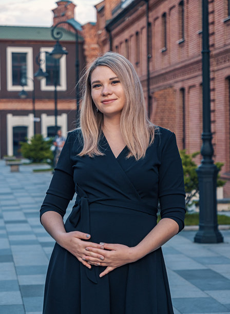 一位身穿黑色连衣裙的年轻孕妇，在日落时分于城镇广场上，自信地在历史悠久的红砖建筑前摆姿势。图片下载