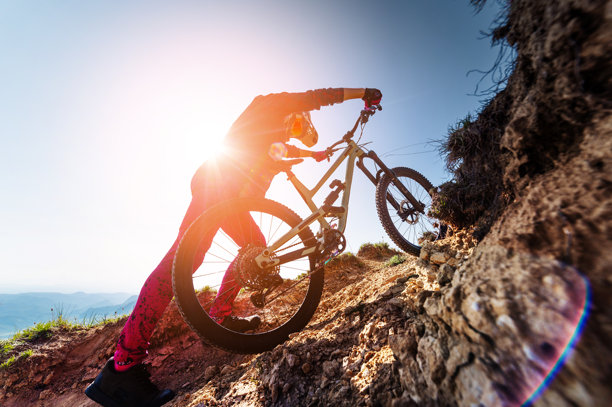 山地车手在崎岖的赛道上。一名男性骑行者推着自行车爬上悬崖，徒步攀爬。极限运动及其幕后生活图片下载
