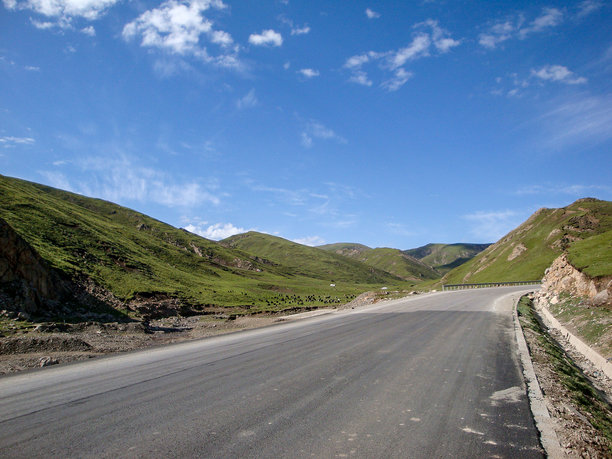 一条风景优美的道路蜿蜒穿过绿色的山地景观，天空湛蓝图片下载