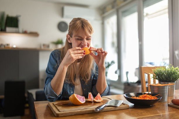 女人在下午放松的居家休闲时刻，在厨房餐桌旁享受新鲜的橙子片图片下载