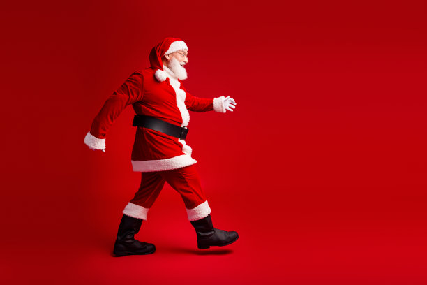 穿着红色服装的圣诞老人走在鲜红的背景上，营造出圣诞和节日季的喜庆氛围的素材照片图片下载