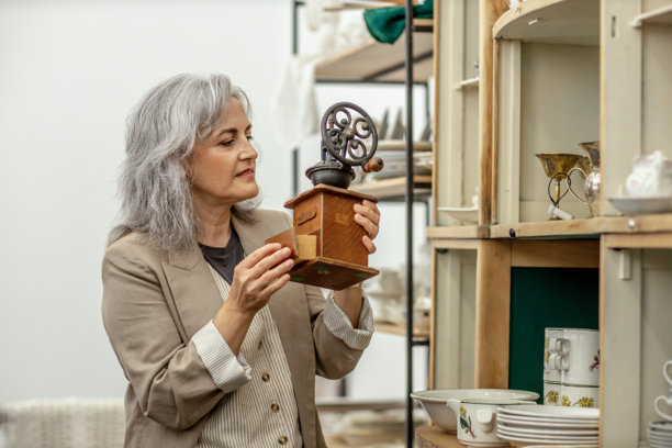 复古仪式：一位成熟的女性在古董店里查看古董咖啡研磨机图片下载