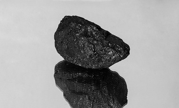 一块煤炭的黑白照片，置于反光表面上。该图像突出了煤炭粗糙的纹理、自然形状和工业象征意义，煤炭常与能源生产、采矿和原始自然资源相关联。图片下载
