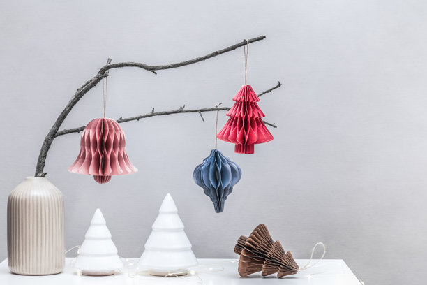 环保可持续圣诞室内装饰。斯堪的纳维亚风格的纸蜂窝装饰放在干树枝上，旁边是陶瓷花瓶和陶瓷圣诞树。图片下载