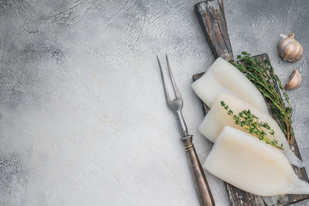 在风化的木板上，新鲜的鱿鱼与香草一同摆放，背景是灰色的石头，非常适合作为海鲜美食的素材概念。图片下载