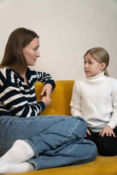 母亲和女儿在家中面对面坐在黄色沙发上，进行着一次衷心的谈话，倾听并给予支持，这是一个坦诚而感人的家庭时刻。竖构图照片图片下载