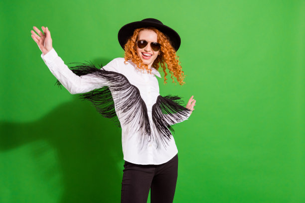 穿着眼镜、帽子和衬衫，留着酷炫橙色发型的女士，在绿色背景上跳舞的照片图片下载