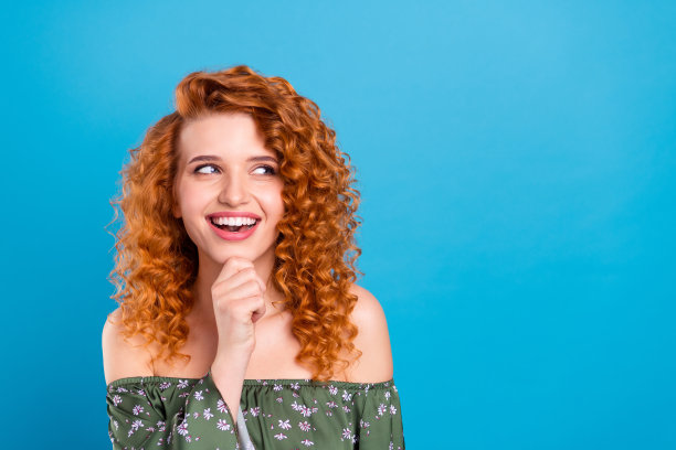 年轻女孩的正面照片，她开心地笑着，手托着下巴，若有所思地望着远方，背景是纯净的蓝色。图片下载