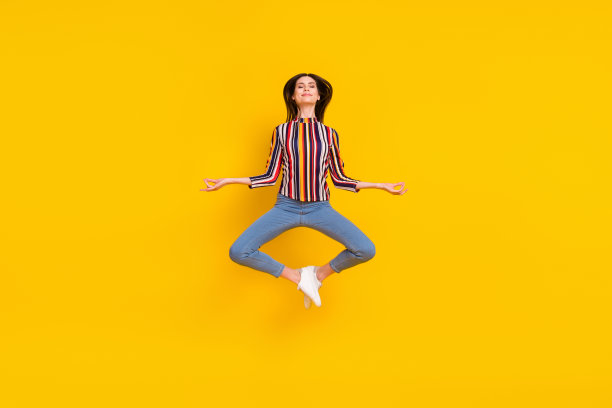 年轻女子身着瑜伽服，面带快乐积极的微笑，在黄色的背景前跳跃冥想，象征着奥姆和平的符号，此为全尺寸照片。图片下载