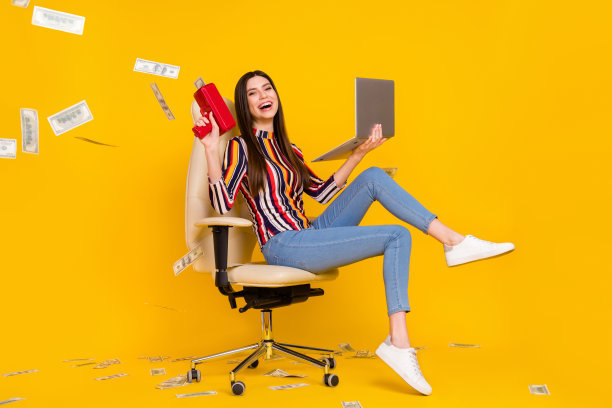 年轻女子全尺寸侧面照片，面带快乐积极的微笑，钱币现金在空中飞舞，笔记本电脑，孤立在黄色背景上图片下载