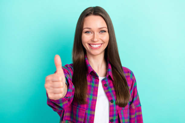 长发千禧一代女士竖起大拇指，身穿格子衬衫，背景是鲜艳的青绿色，照片显示出感激之情图片下载
