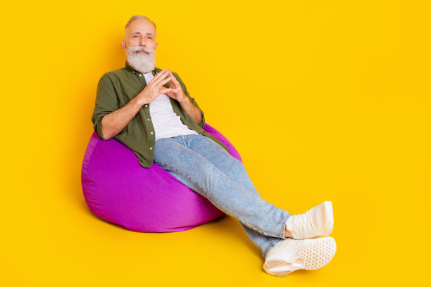 照片：一位穿着绿色衬衫、坐在懒人沙发上的酷炫成熟男性，手指交握，看向镜头，背景为黄色。图片下载