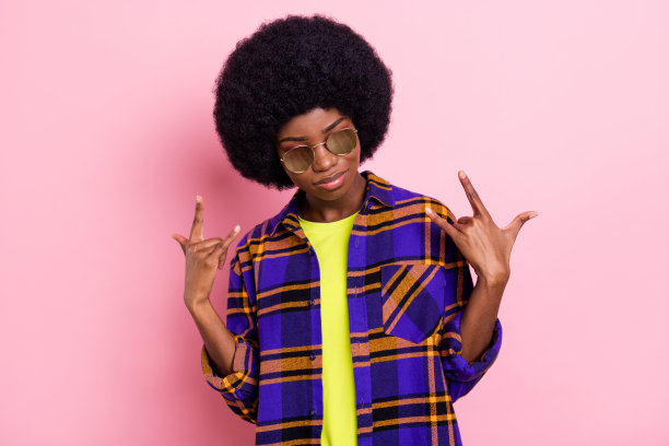 粉彩粉色背景下，一位迷人、严肃、酷炫的女孩，比出摇滚手势，其余部分静止。图片下载