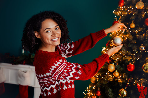 一位穿着红色圣诞毛衣的俏皮女子在温馨的家中装饰发光的圣诞树，营造节日气氛的素材照片图片下载