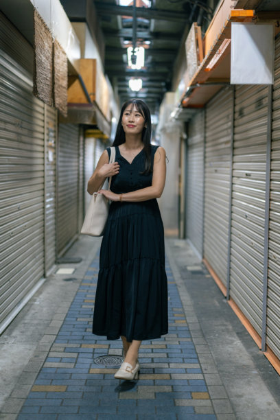 身着黑裙的女子走在狭窄的商业街上，所有卷帘门都已关闭图片下载