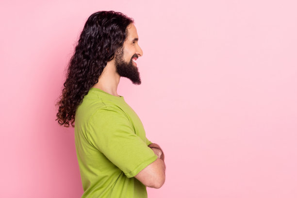 一个人侧面肖像照，他有着迷人的男性化、快乐的长发，双臂交叉，背景为粉红色，有复制空白空间图片下载