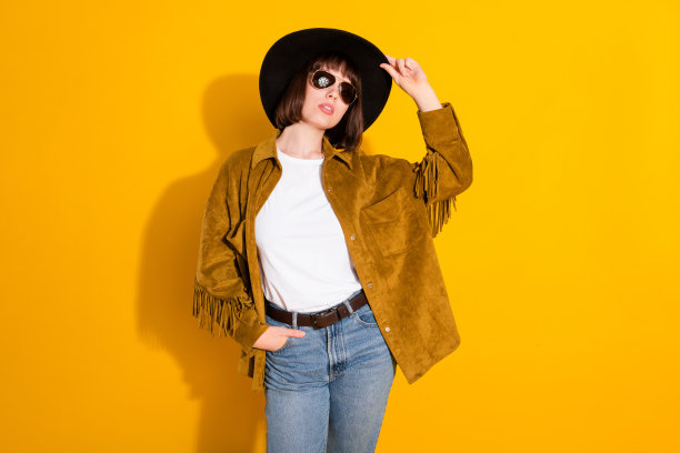 身穿牛仔装、戴着墨镜、戴着头饰的酷炫漂亮年轻女子，在孤立的黄色背景前。图片下载