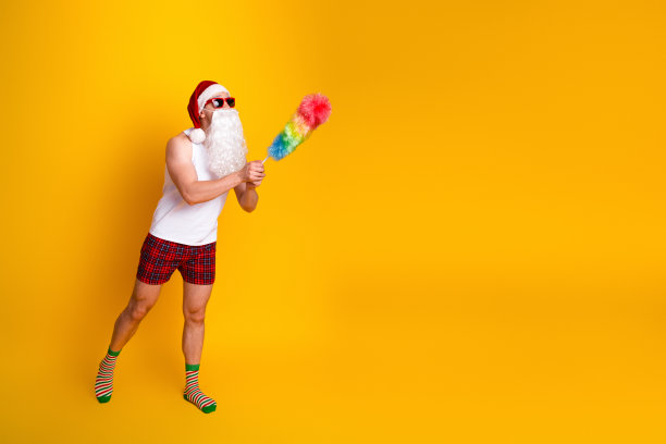 身穿休闲装、手持彩虹掸子的俏皮圣诞老人，在明亮的黄色工作室里，用节日的幽默感和假日氛围点亮了场景，适合用作素材图。图片下载