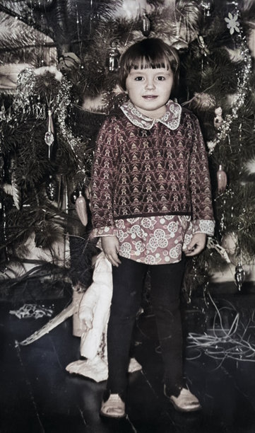 一张复古风格的可爱三岁小女孩站在圣诞树旁的肖像照。摄于 1970 年。图片下载