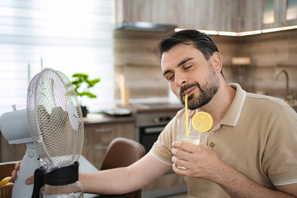 夏日居家酷暑，男子在家中喝柠檬水并用电风扇纳凉图片下载