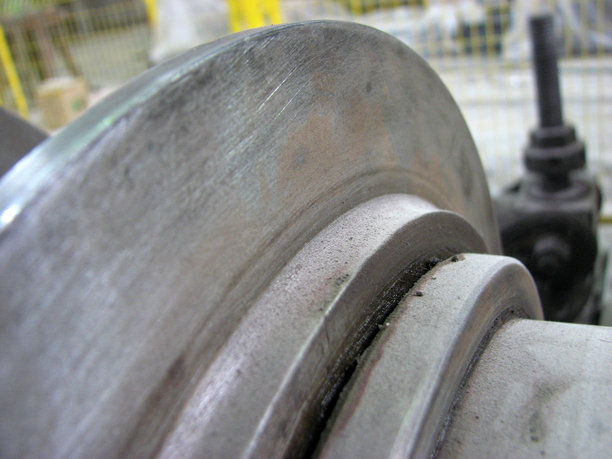 一张特写微距照片，展示了一个磨损严重、带有划痕、凹槽以及油污痕迹的金属零件。背景中工业环境模糊不清。图片下载