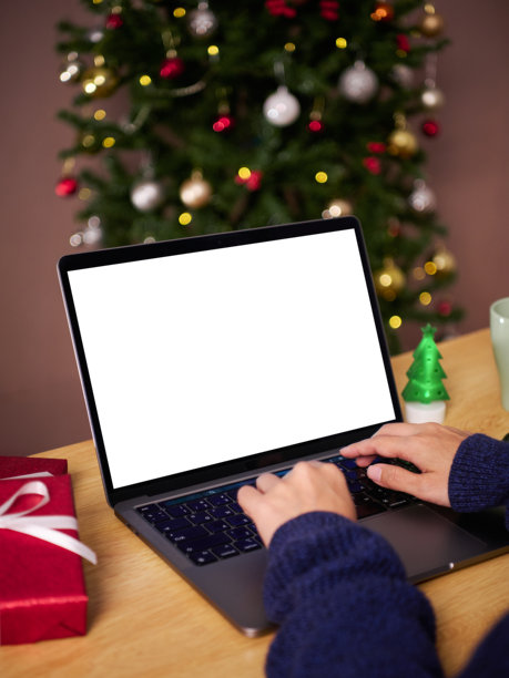 圣诞办公室节日工作空间，一人正在笔记本电脑上打字，屏幕空白，代表在线庆祝、数字沟通、远程工作、生产力、节日季和创意。图片下载