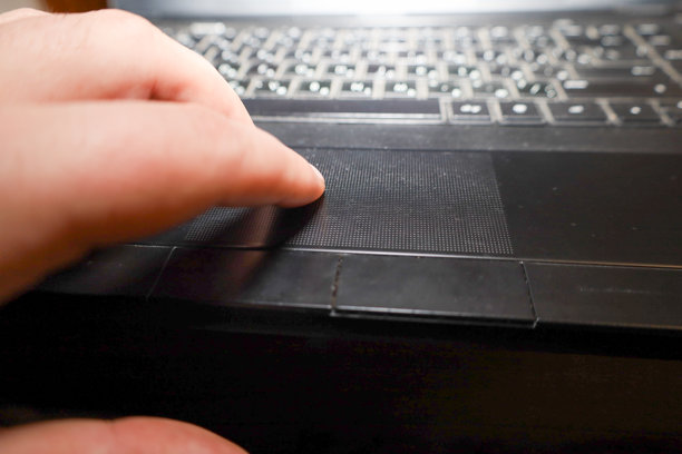 特写镜头展示了一台黑色笔记本电脑的局部：用户的手指触碰着触摸板，用它来控制电脑。这张图片强调了在工作或学习过程中人与技术的互动。图片下载