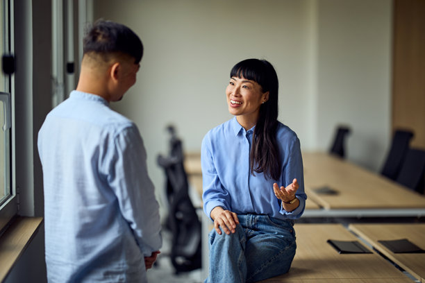 在轻松的商务会议中，一位亚洲女性和一位亚洲男性在现代办公室工作空间里进行讨论图片下载
