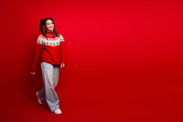 穿着红色圣诞毛衣的年轻女子在红色背景上行走，面带微笑，充满节日气息的时尚素材照片图片下载
