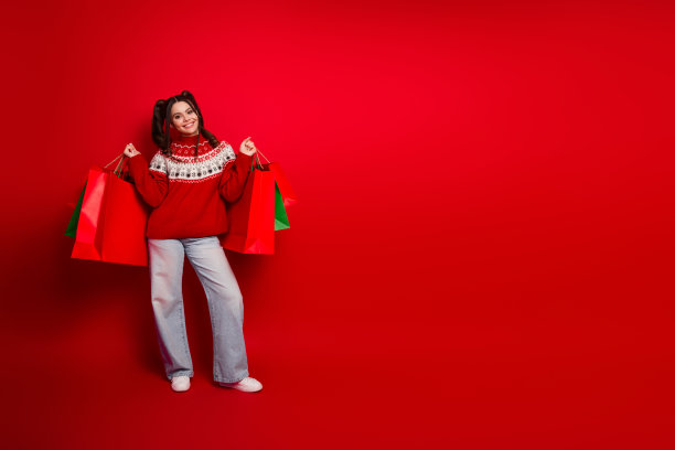 身穿红色圣诞毛衣的购物女孩，手持彩色购物袋，背景为红色，呈现节日的购物生活方式。这张图片适合用作素材。图片下载