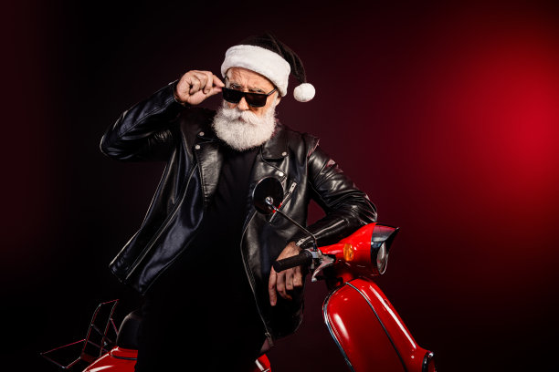 身穿皮夹克的摇滚风圣诞老人骑着红色摩托车，摆出酷炫的节日造型，进行现代假日拍摄图片下载