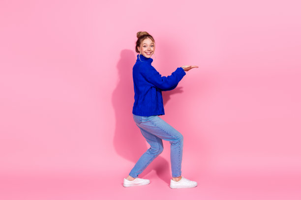 年轻女子身穿蓝色毛衣，在粉色背景前微笑，适合生活方式时尚图库照片图片下载