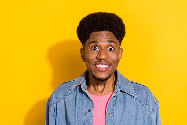 一名身穿牛仔衬衫、戴着大眼睛、脸上带着令人印象深刻的酷炫表情的深肤色男子，面带微笑，背景为孤立的黄色。图片下载