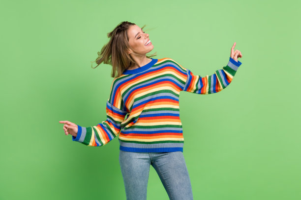 照片肖像：女孩在派对上放松地跳舞，穿着条纹毛衣和牛仔裤，背景是孤立的粉彩色绿色图片下载