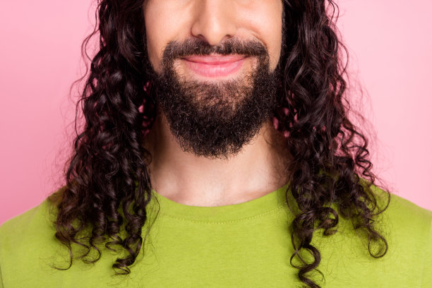 照片：一个留着胡须、穿着绿色T恤、面带微笑的迷人帅气年轻男子，背景为孤立的粉红色图片下载