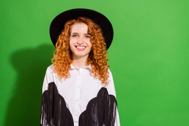 一位迷人的、快乐的、波浪卷发的女孩，身着时髦酷炫的牛仔装扮，在明亮的绿色背景前摆出肖像姿势。图片下载