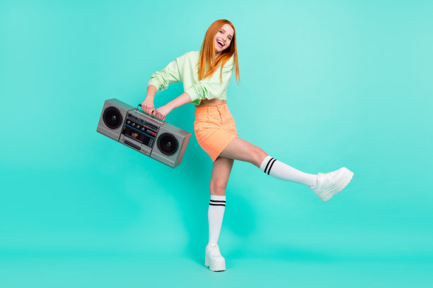 全身照，漂亮的红发女孩，手持复古录音机，在鲜艳的绿松石色背景下跳舞图片下载