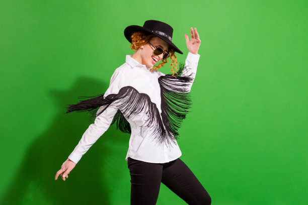 戴着眼镜、帽子和衬衫，留着姜黄色头发的女士，穿着舞服，在绿色背景前欢呼雀跃，这是她的个人资料照片图片下载